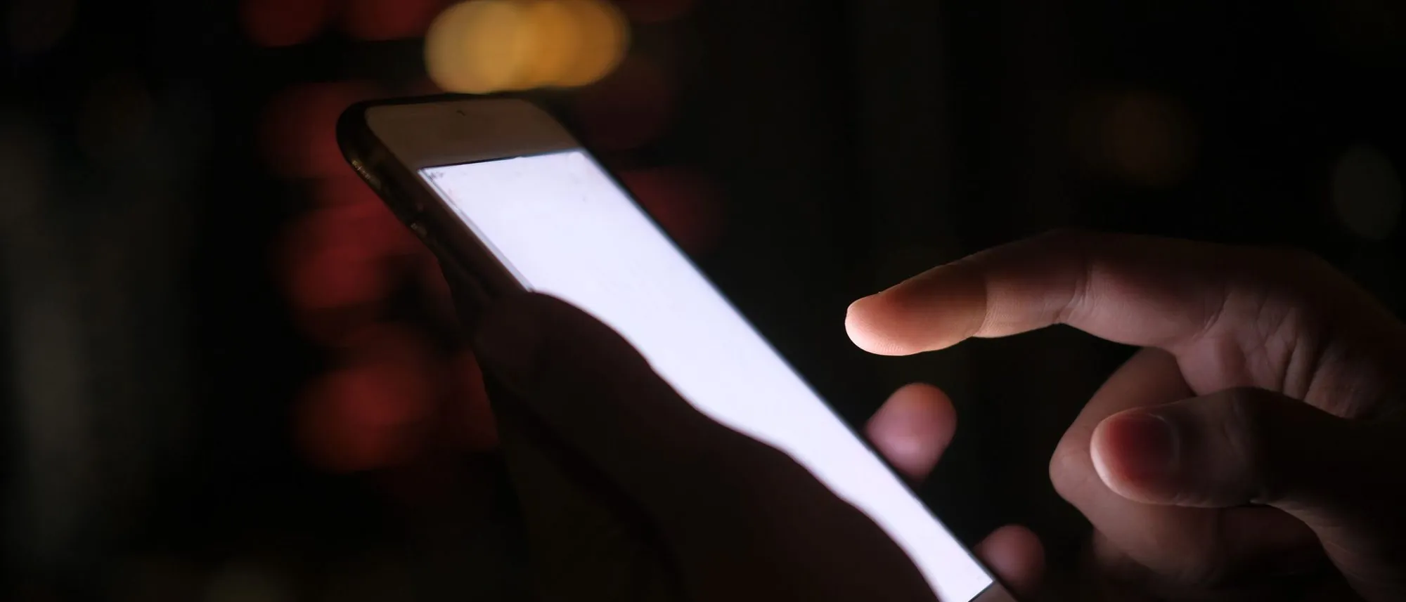 A hand holds a lit smartphone at night against blurred city lights.