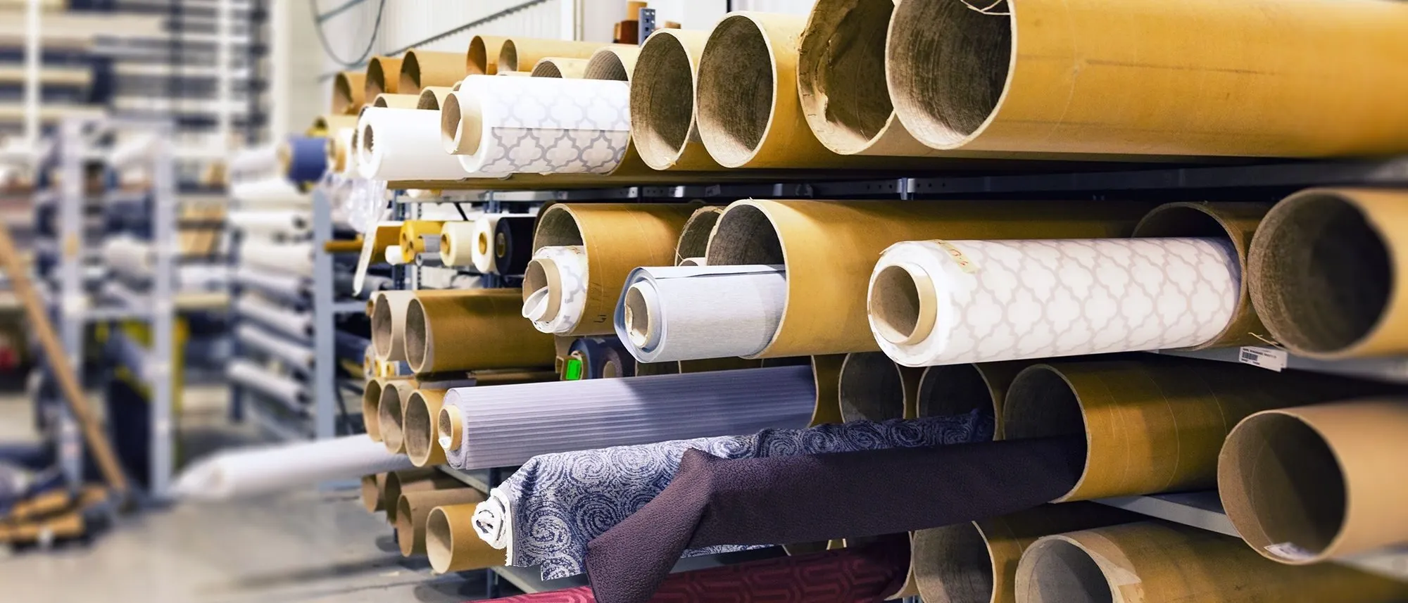 Rows of rolled textiles stored on their sides in a factory, seen at shallow depth of field.